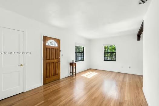 Wood-finish flooring, white walls, wood-paneled entry door with decorative glass inlay, and grid-pattern window panes
