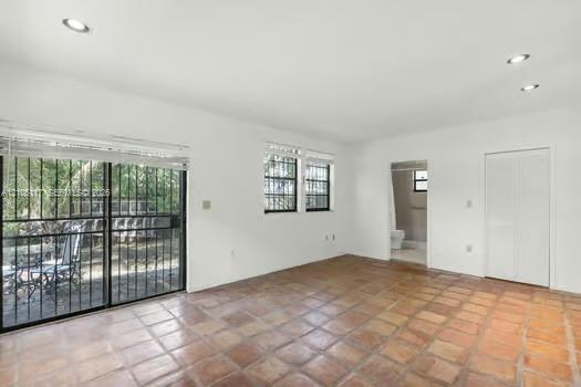 Spacious room featuring terra-cotta tile flooring, recessed lighting, white louvered closet doors, and a sliding glass door with integrated security bars