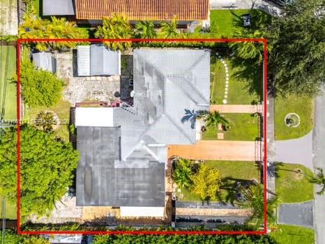 Aerial view featuring a multi-section roofline, paved driveway, detached storage structure, mature landscaping, and an enclosed backyard