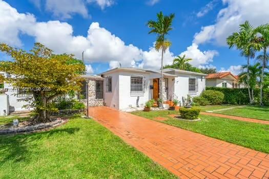 Exterior facade featuring white stucco finish, stone masonry accents, a terra-cotta brick driveway, window security bars, and mature palm trees