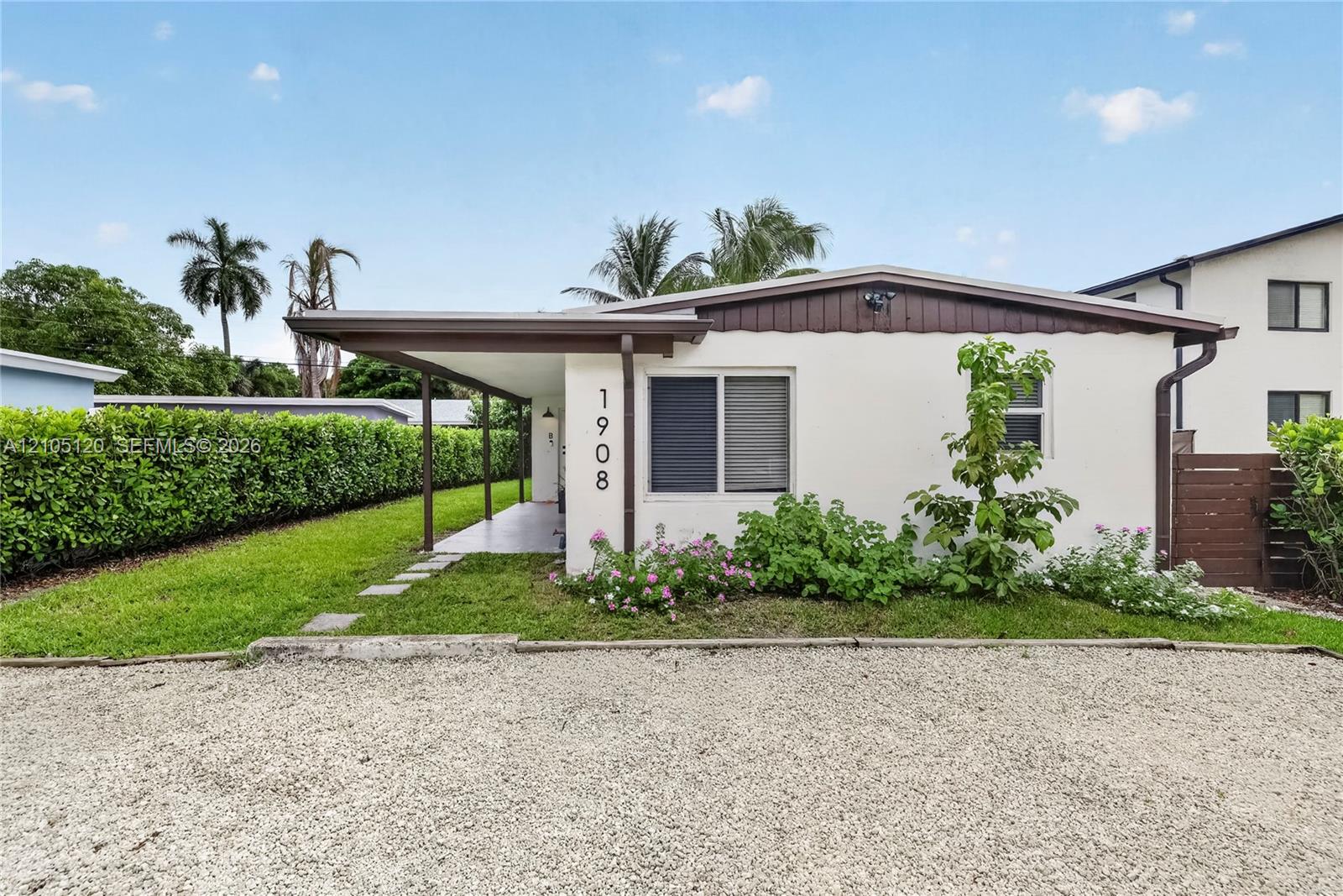 Exterior featuring a stucco facade, covered porch, gravel driveway, and landscaped perimeter with mature hedging