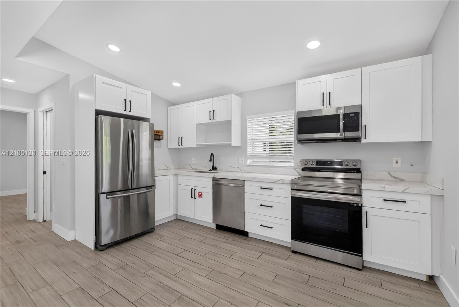 Kitchen featuring white shaker cabinetry, stainless steel appliances, stone-patterned countertops, recessed lighting, and wood-finish flooring
