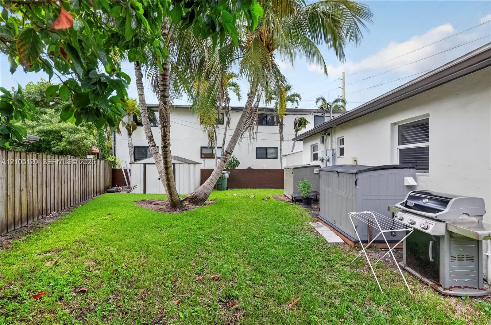 Fenced backyard featuring a manicured lawn, mature palm trees, and structural storage units
