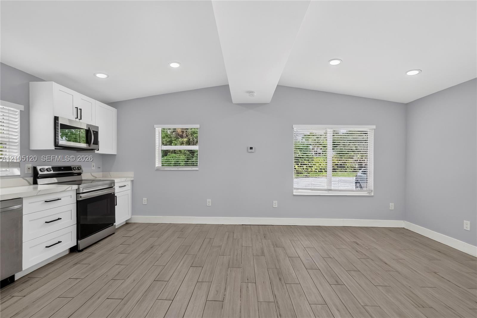Kitchen featuring white Shaker-style cabinetry, stainless steel appliances, wood-finish tile flooring, recessed lighting, and a vaulted ceiling