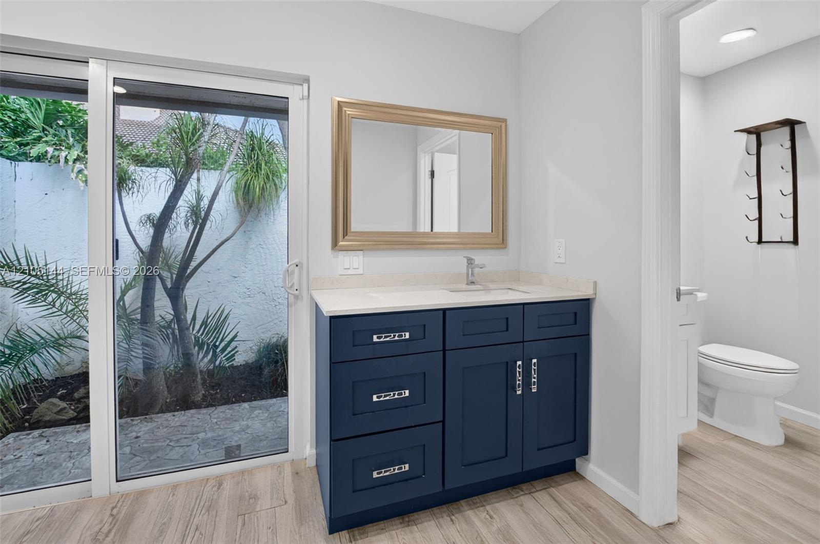 Navy blue vanity with light-toned stone countertop, integrated rectangular sink, framed mirror, and sliding glass door with external patio access