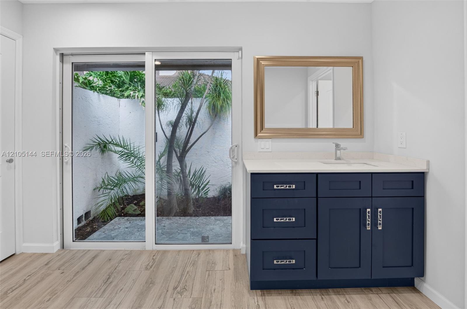 Dark blue shaker-style vanity with a light-toned countertop, integrated basin, silver-finish hardware, and wood-finish flooring, featuring sliding glass doors to a private exterior patio