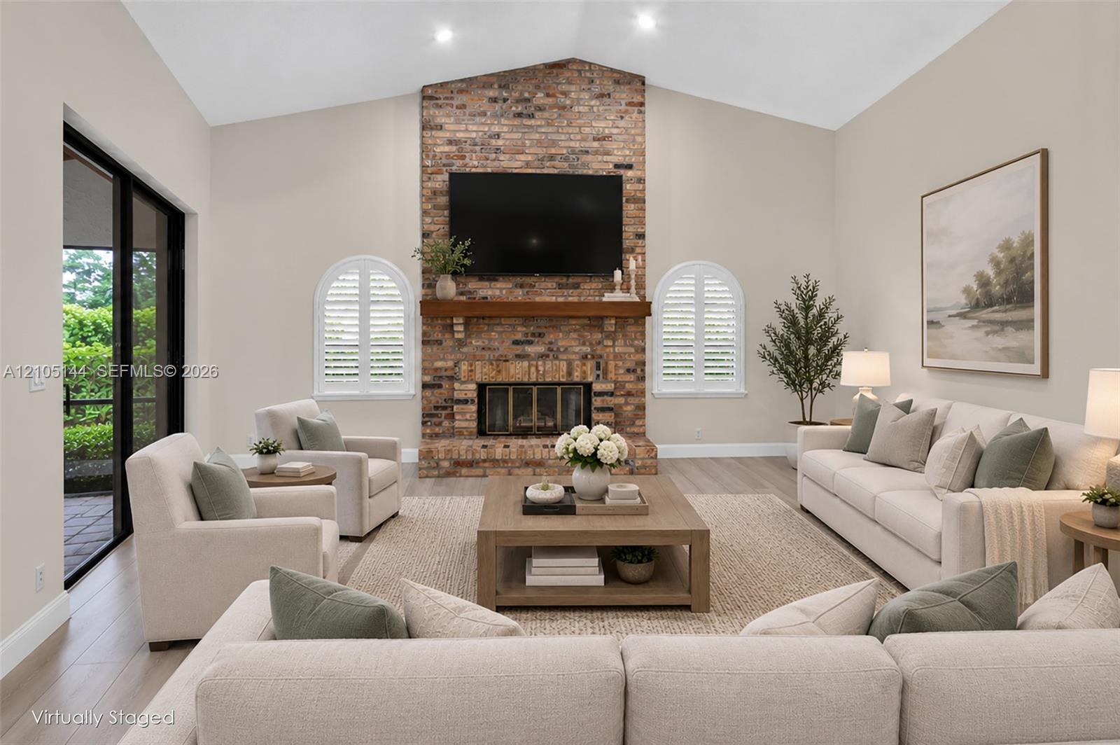 Vaulted ceilings, full-height brick fireplace, wood-finish mantel, arched windows with plantation shutters, and sliding glass doors