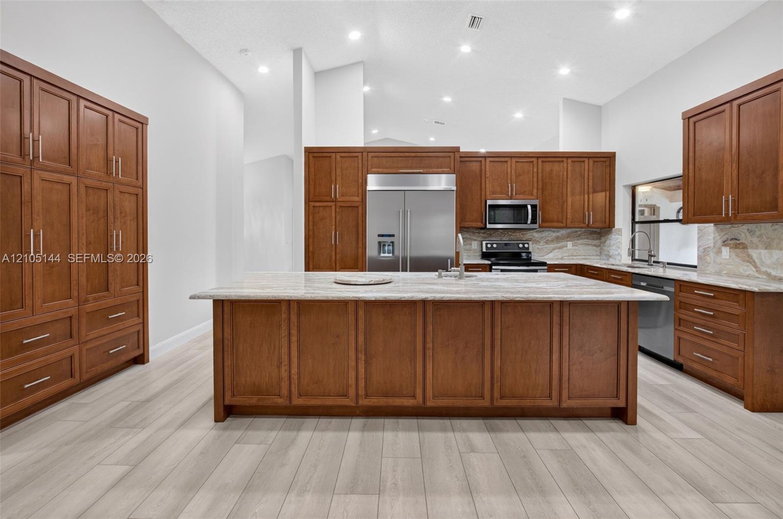 Kitchen featuring custom wood cabinetry, central island with stone countertop, stainless steel appliances, and wood-finish flooring under recessed lighting