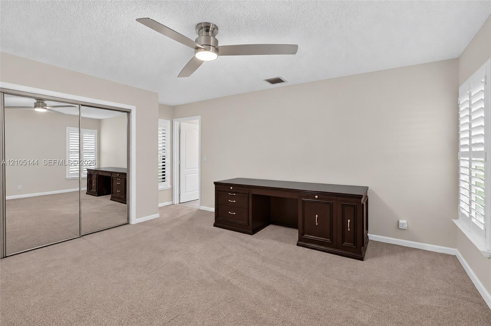 (FAN VIRTUALLY STAGED AS SIMILAR PIECE WILL BE INSTALLED) Bedroom featuring neutral carpet, mirrored sliding closet doors, a ceiling fan with integrated lighting, and white plantation shutters