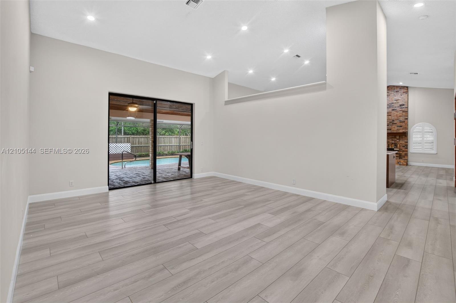 Open living area featuring wood-finish flooring, recessed lighting, high ceilings with architectural cutouts, sliding glass doors, and a brick-accented interior wall