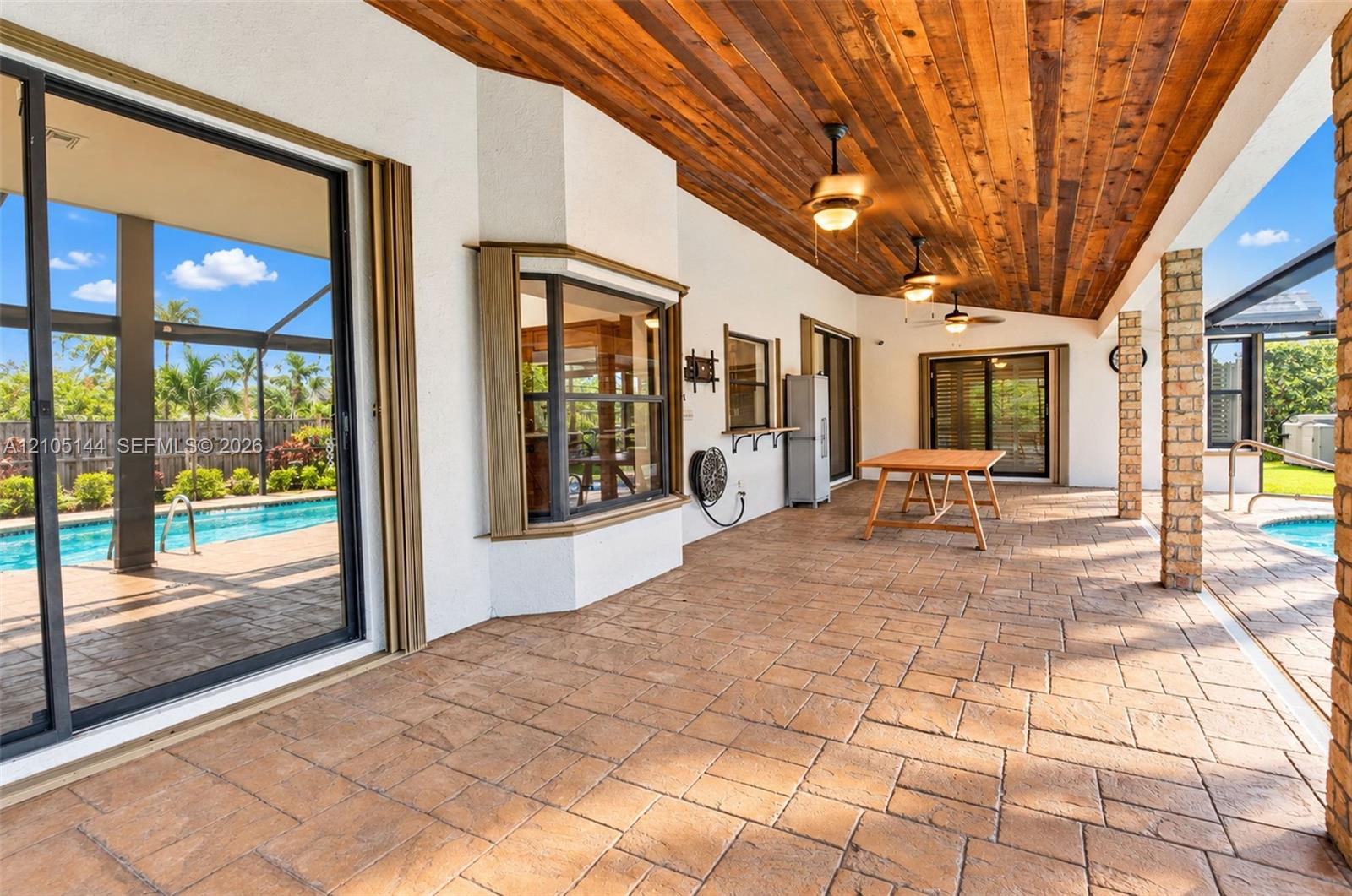Covered lanai featuring a tongue-and-groove wood ceiling, stamped concrete flooring, brick pillars, and sliding glass door access