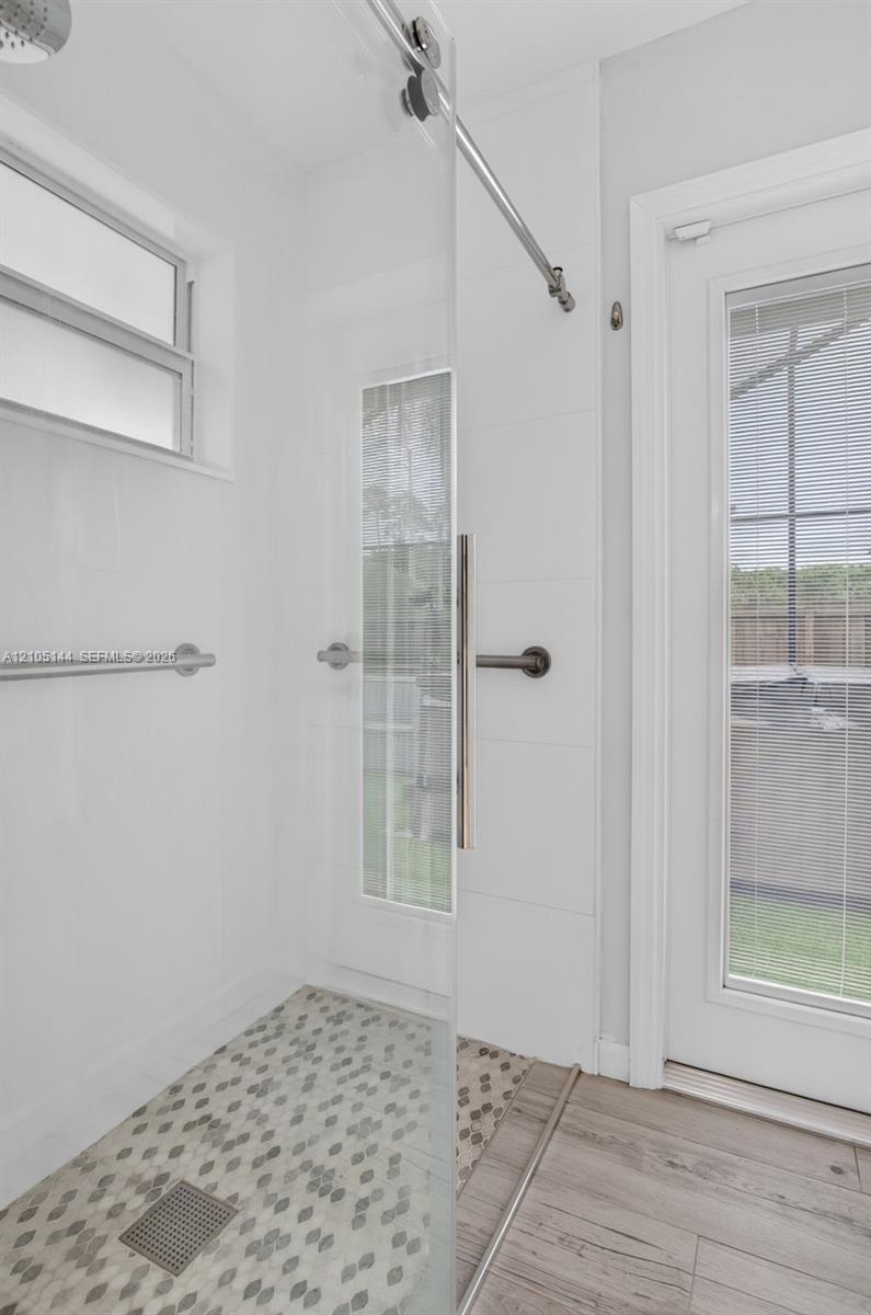 Walk-in shower featuring a sliding glass door, hexagonal tile flooring, wall-mounted brushed metal hardware, and a rainfall shower head