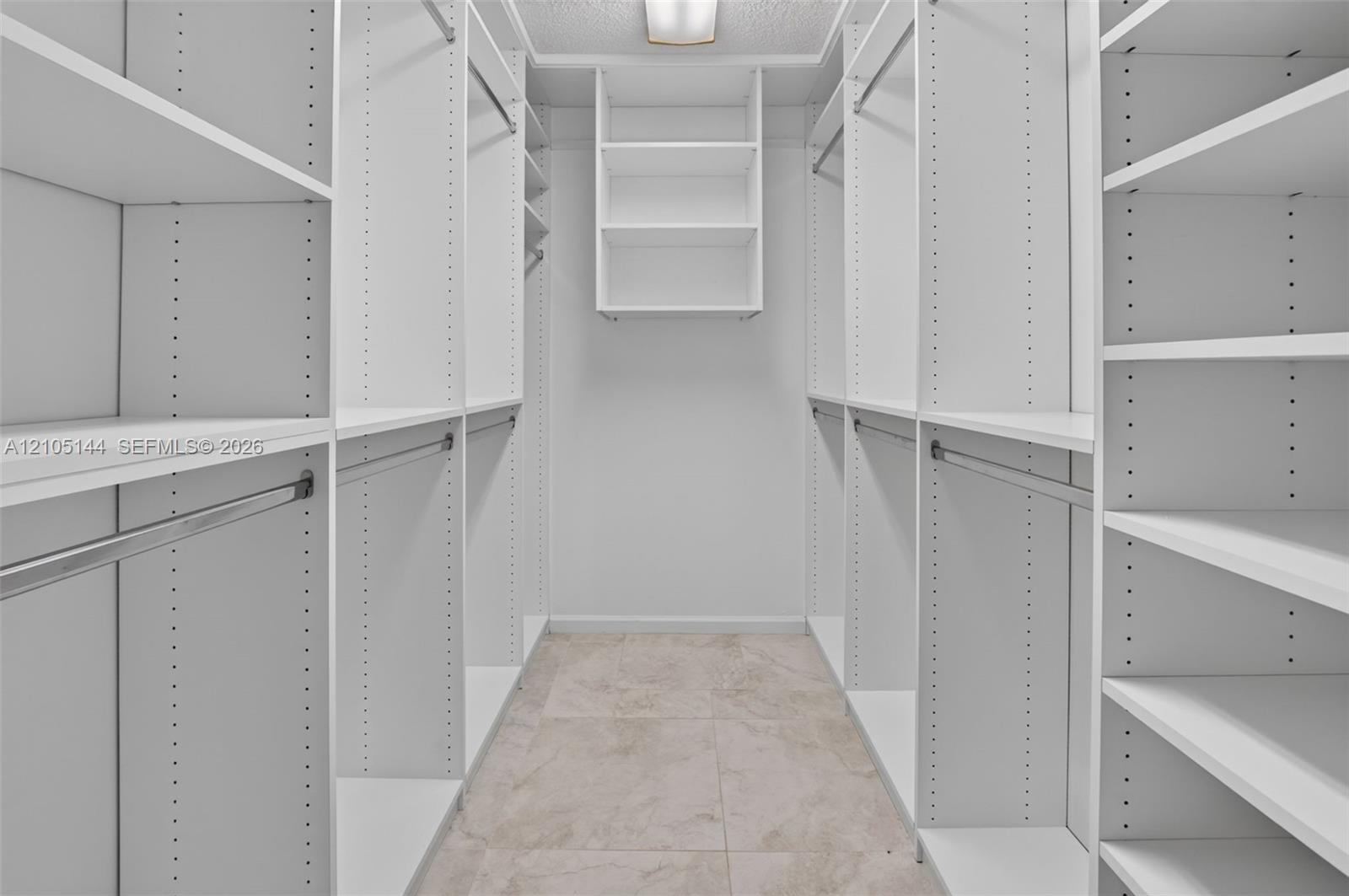 Walk-in closet featuring white built-in shelving, adjustable shelf tracks, metal garment rods, and tile flooring