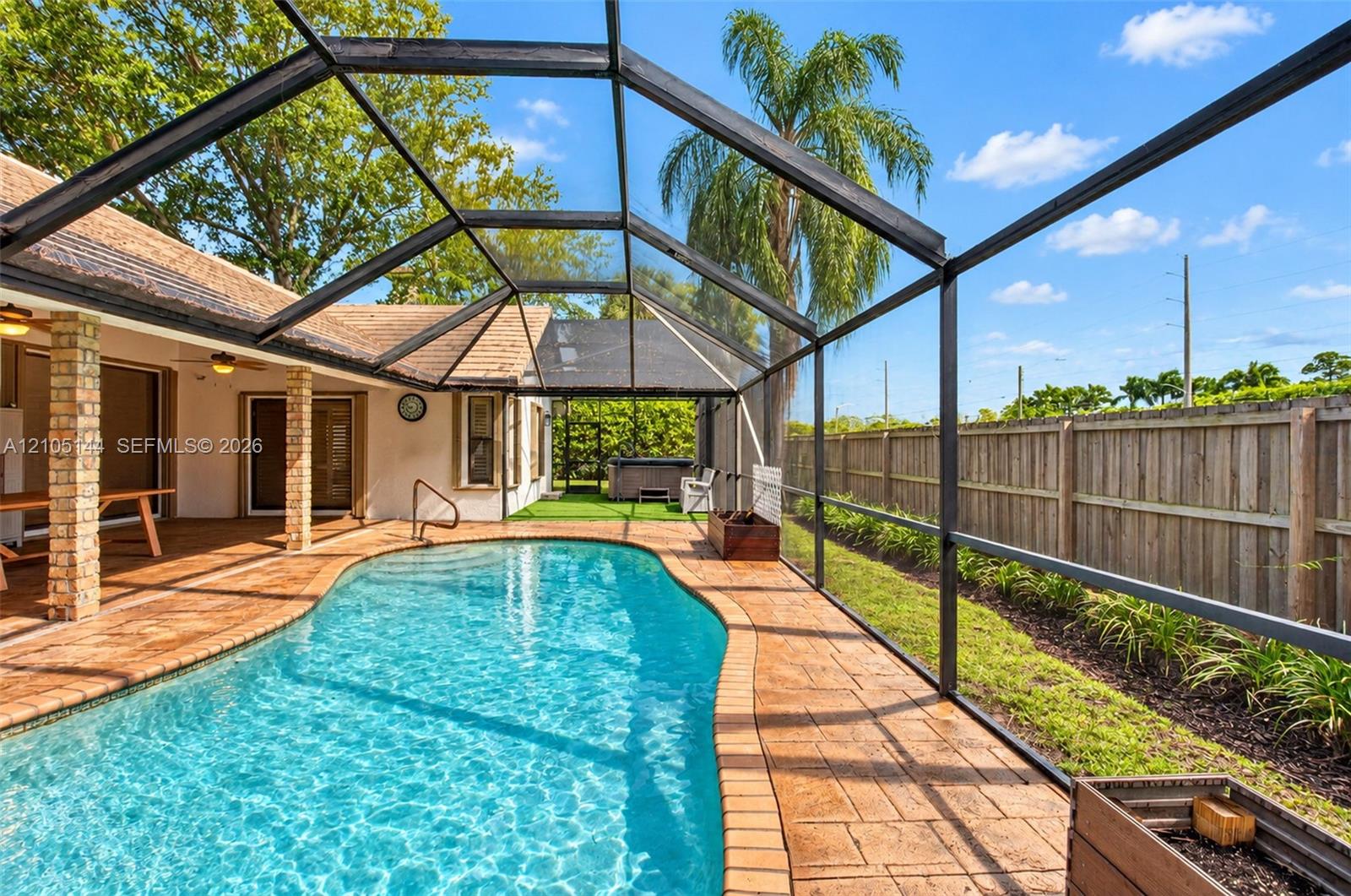 Screen-enclosed pool featuring a stamped concrete deck, brick-columned covered lanai, and wood privacy fencing