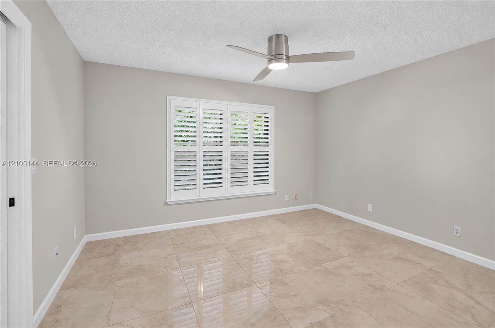 (FAN VIRTUALLY STAGED AS SIMILAR PIECE WILL BE INSTALLED)Neutral interior featuring large-format tile flooring, crisp neutral wall paint, white plantation shutters, and a modern brushed-metal ceiling fan with integrated lighting