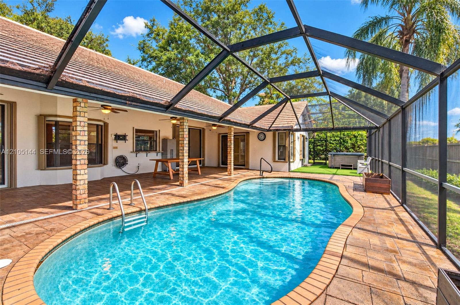 Screen-enclosed patio area featuring a free-form swimming pool, brick-paver decking, covered lanai with exposed brick columns, and a built-in spa