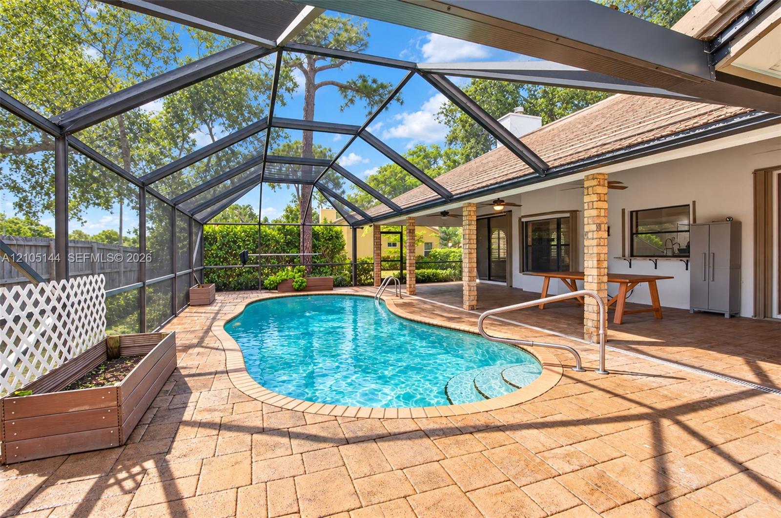 Screened-in patio featuring a paver deck, kidney-shaped pool, brick-clad support columns, and built-in planters
