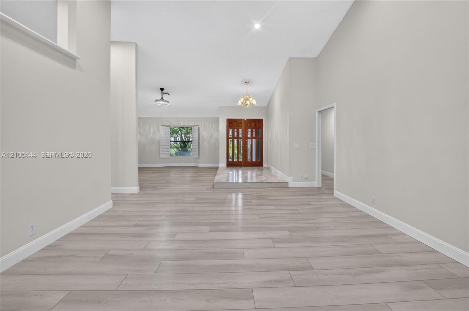 Open interior featuring vaulted ceilings, wood-finish flooring, double-door entryway, elevated stone-finish foyer landing, and a bay window