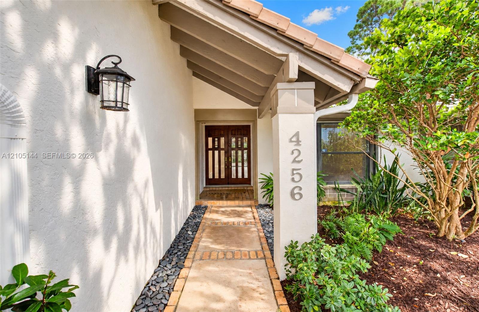 Covered entryway featuring a concrete paver walkway, stucco exterior, decorative wall-mounted light fixture, and double entry doors with vertical glass panes