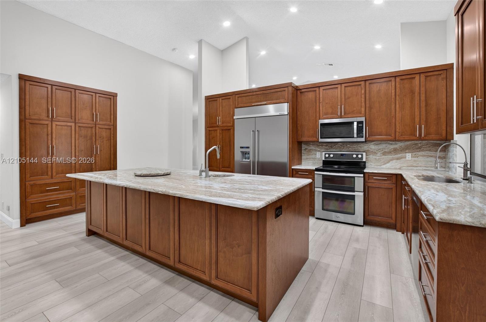 Kitchen featuring wood cabinetry, large central island, stone countertops, stainless steel appliances, and wood-finish flooring