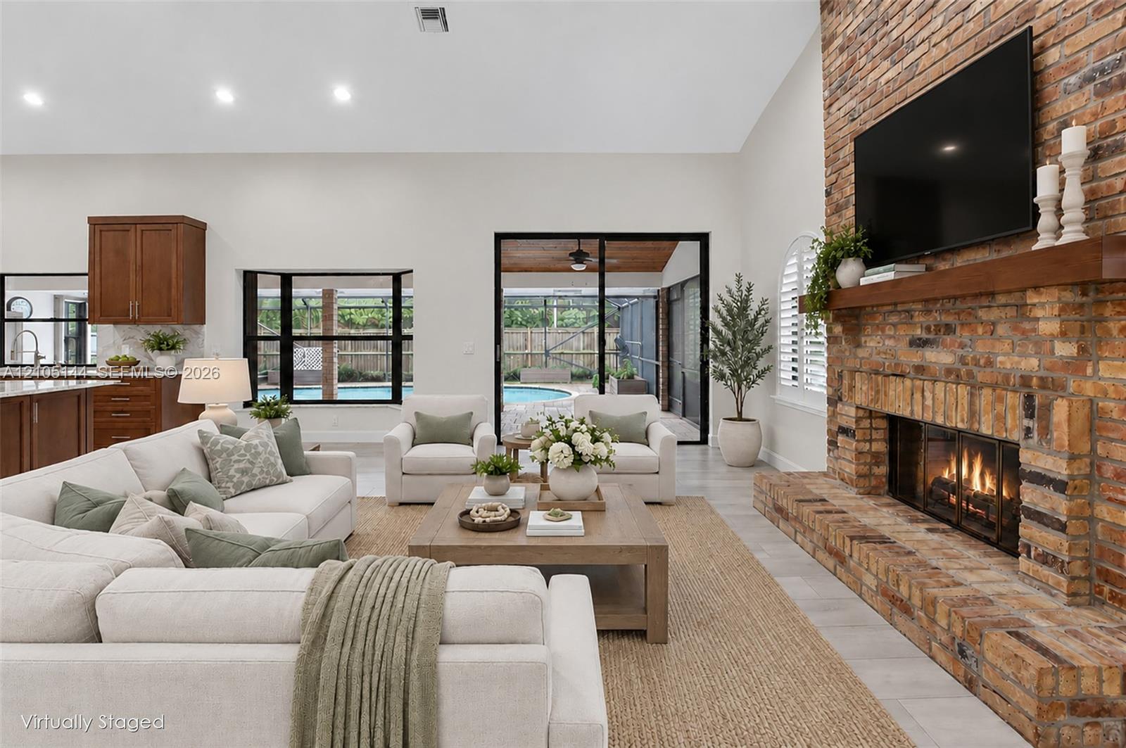 Vaulted ceilings, floor-to-ceiling brick fireplace with a wood mantel, recessed lighting, expansive glass sliding doors, and wood-finish flooring