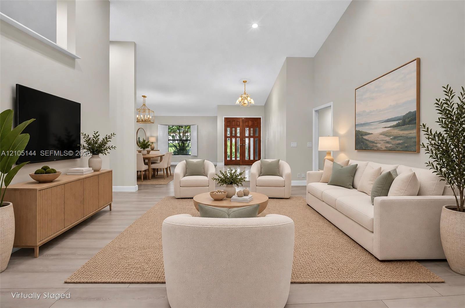 Spacious interior featuring vaulted ceilings, neutral wall tones, light wood-finish flooring, double front entry doors with glass panels, and multiple hanging pendant light fixtures