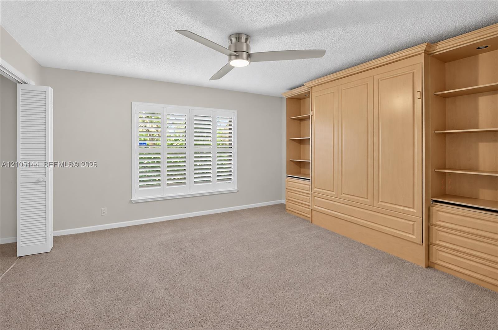 (FAN VIRTUALLY STAGED AS SIMILAR PIECE WILL BE INSTALLED) Custom light-toned built-in cabinetry, window with plantation shutters, ceiling fan with integrated lighting, and louvered closet doors