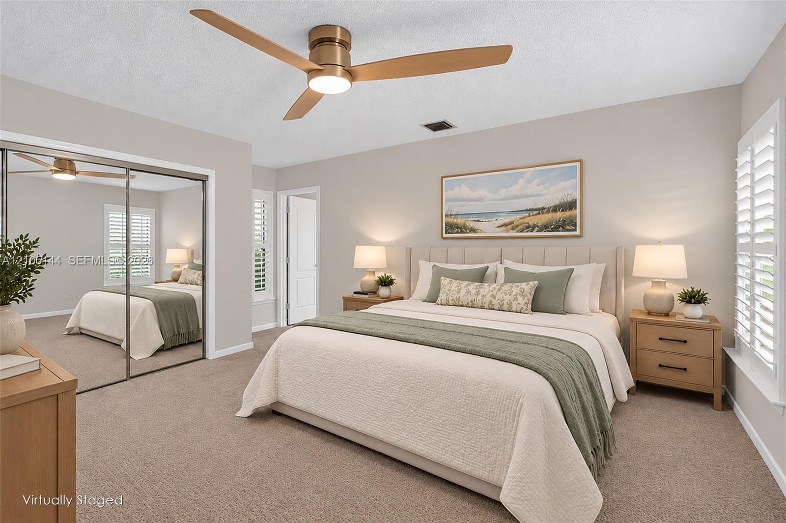 Neutral-toned interior featuring wall-to-wall carpeting, floor-to-ceiling mirrored closet doors, a brushed metal ceiling fan with integrated lighting, and white plantation shutters