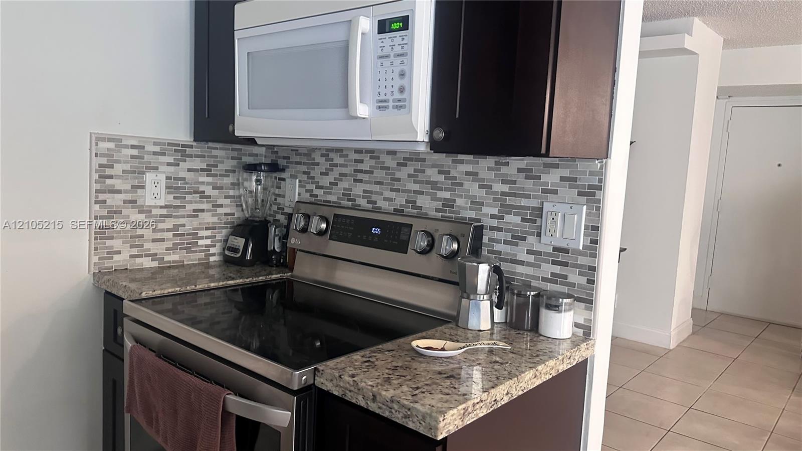 Kitchen featuring dark cabinetry, stone-finish countertops, stainless steel range, white over-the-range microwave, and a multicolored glass tile backsplash
