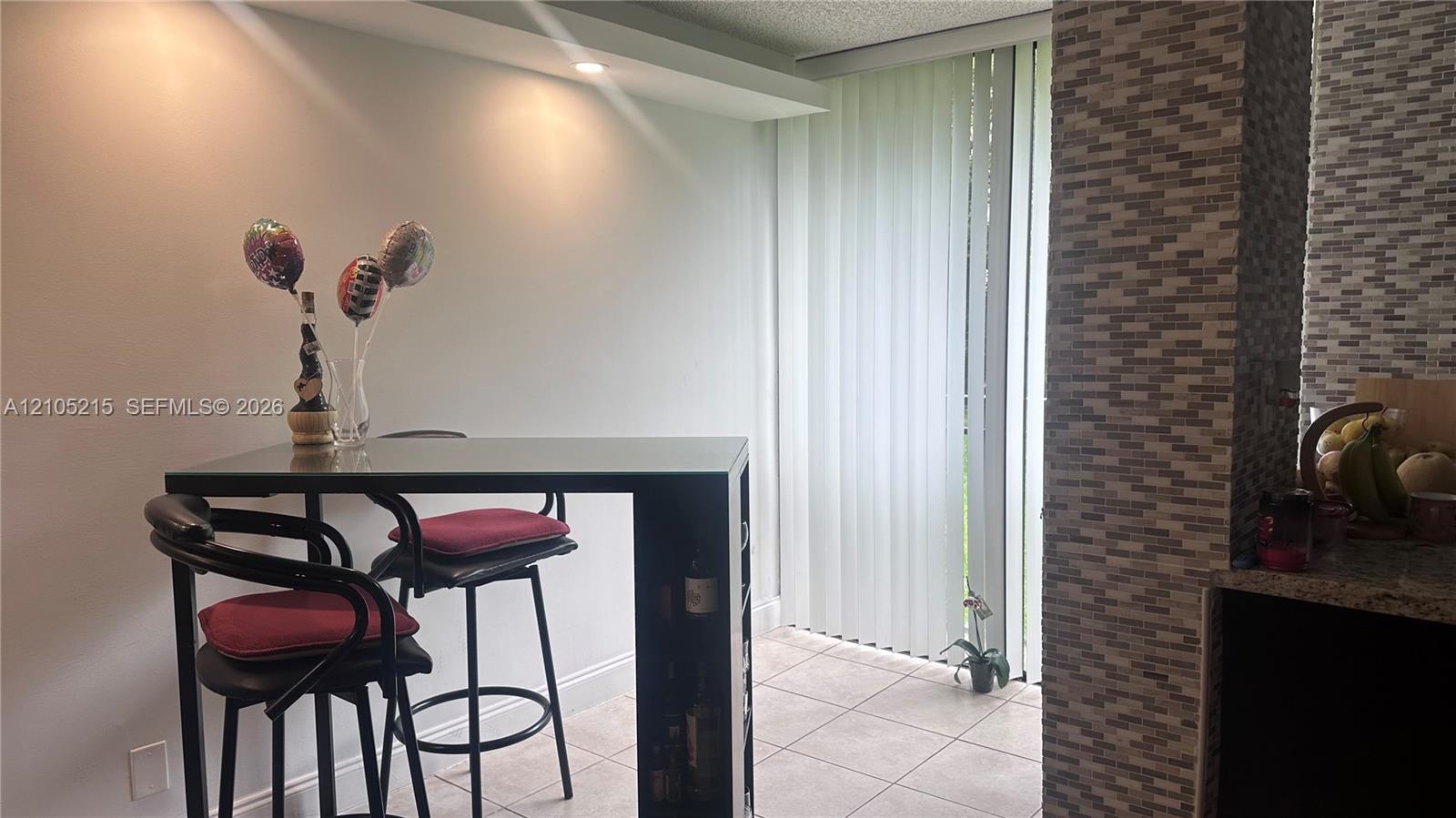 Vertical blind window treatment, textured tile accent wall, recessed ceiling lighting, and ceramic tile flooring
