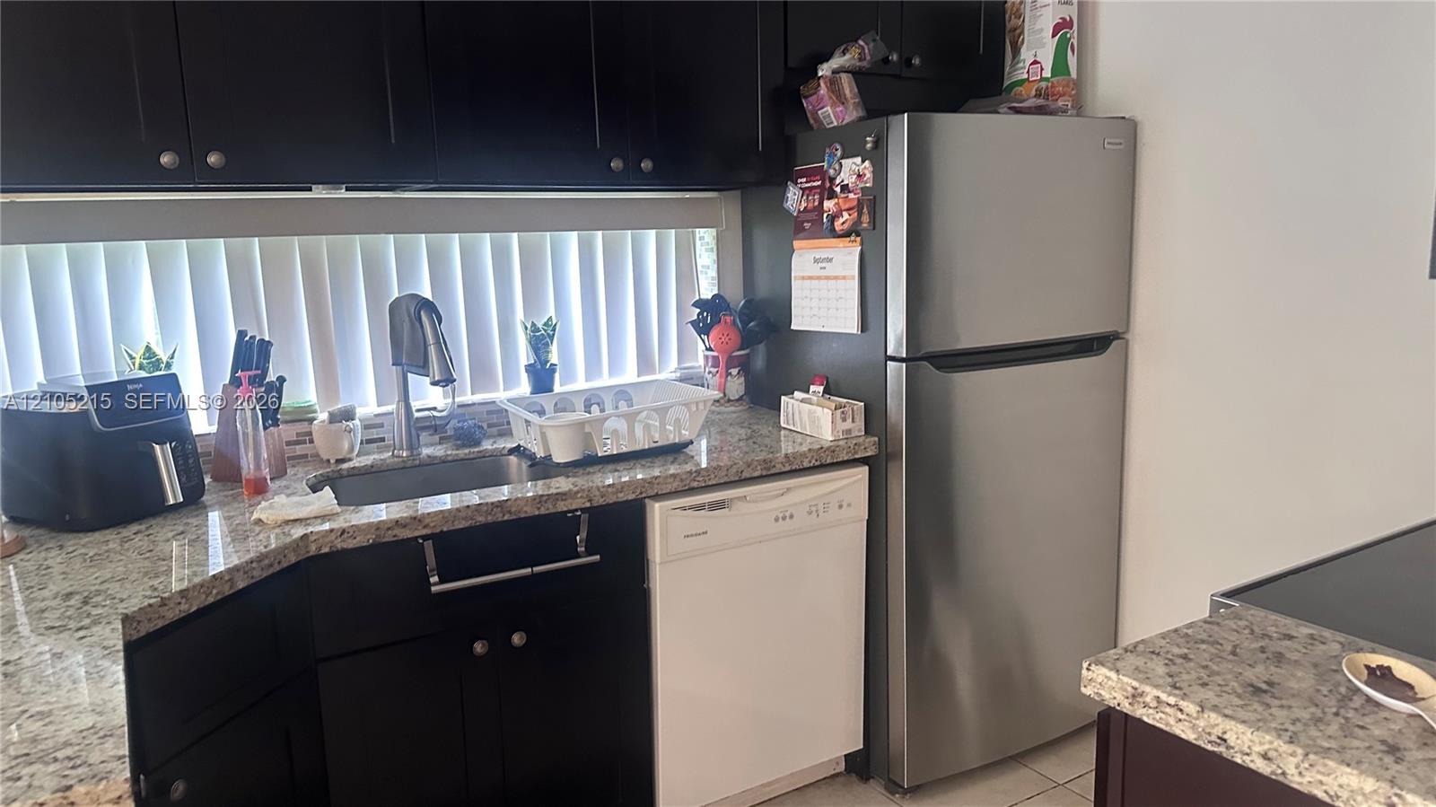 Kitchen featuring dark cabinetry, stone-finish countertops, stainless steel refrigerator, and undermount sink with a gooseneck faucet
