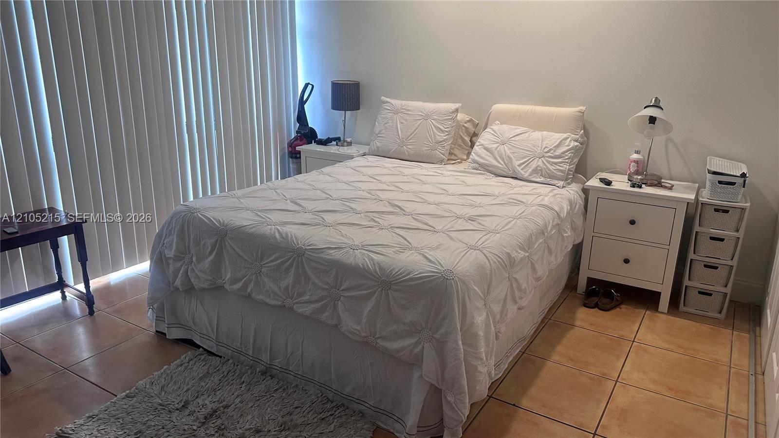 Room featuring large-format ceramic floor tile and vertical blinds covering the window wall