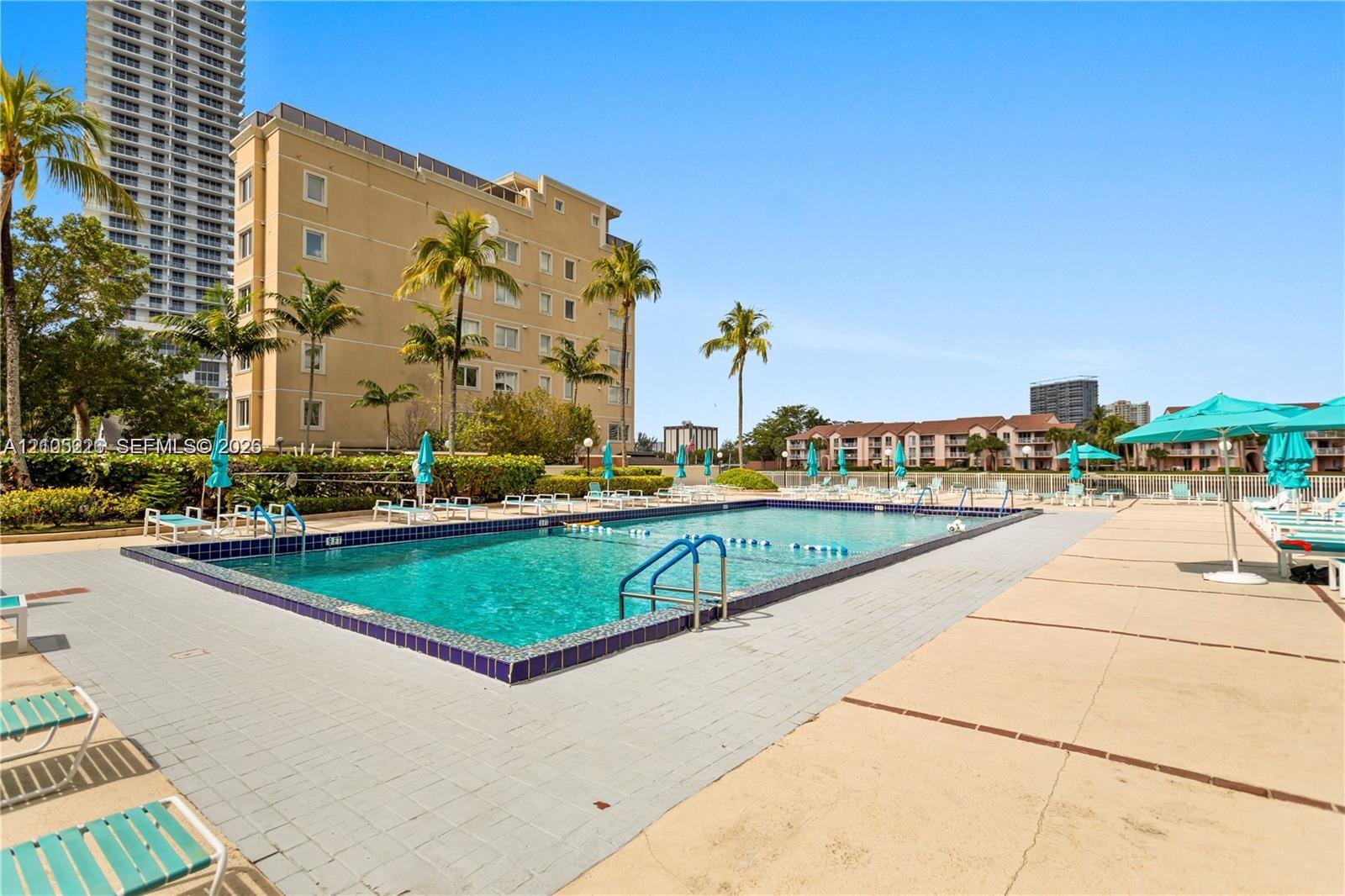 Rectangular swimming pool featuring a tiled waterline, metal handrails, a paved perimeter, and surrounding palm trees