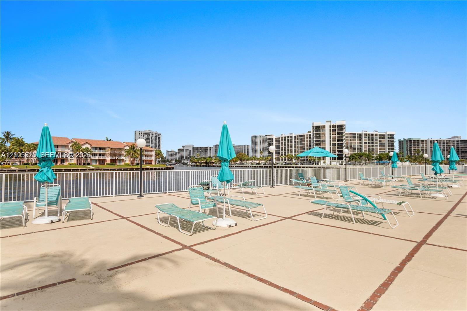 Outdoor swimming pool featuring a tiled waterline, metal handrails, and a surrounding paved deck with mature palm trees