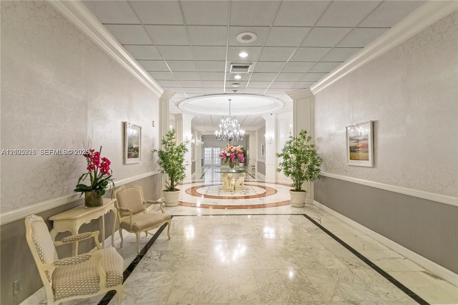 Polished stone flooring with decorative inlay, intricate ceiling chandelier, recessed lighting, and crown molding