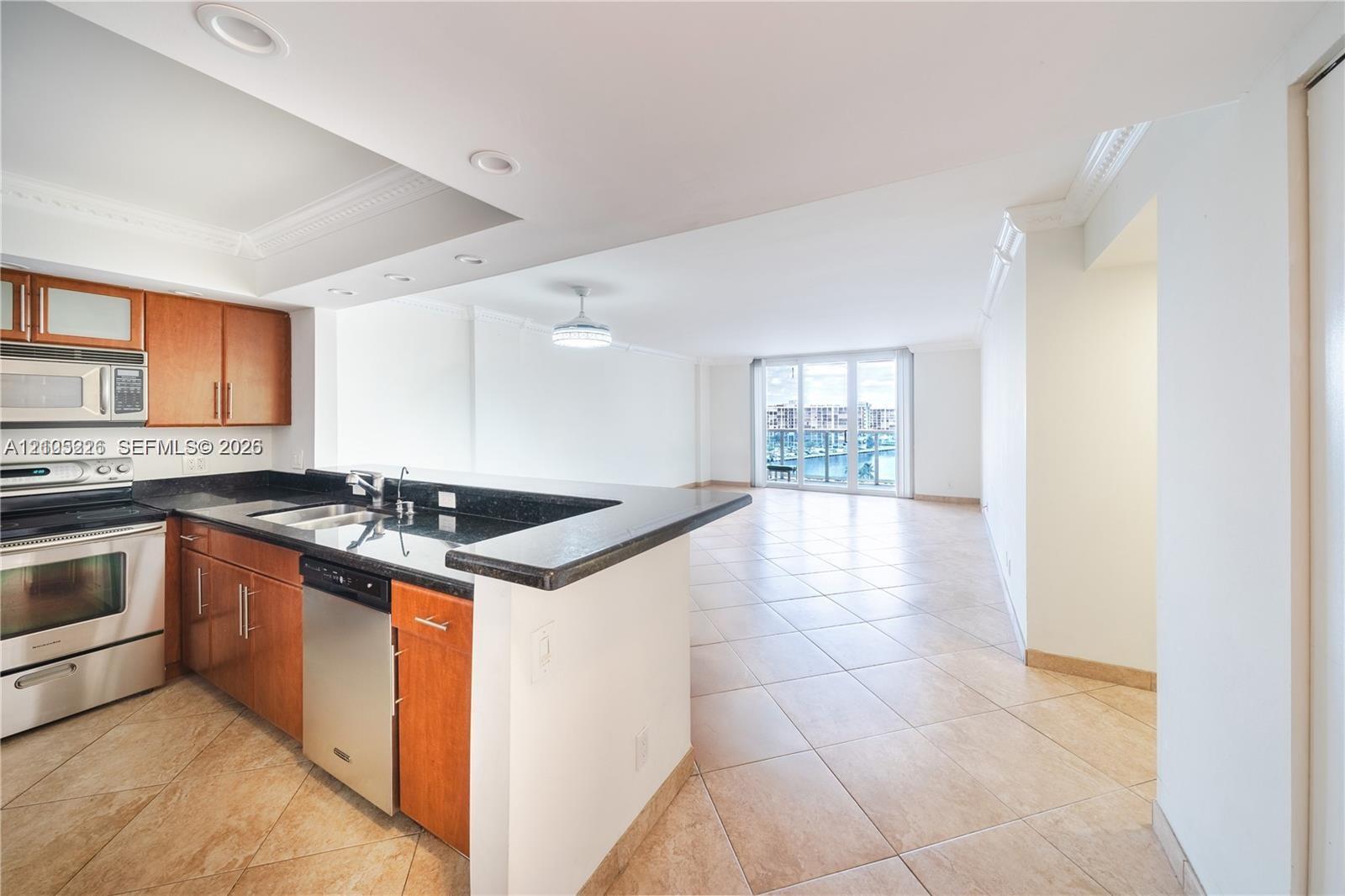 Open floor plan featuring large-format tile flooring, crown molding, and a peninsula-style kitchen counter with built-in cabinetry