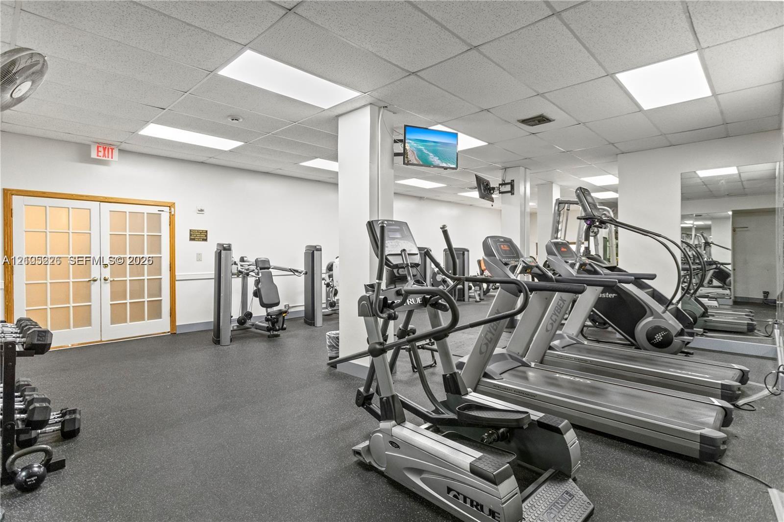 Fitness area featuring durable rubber flooring, a drop-ceiling grid with recessed lighting, and white structural support columns