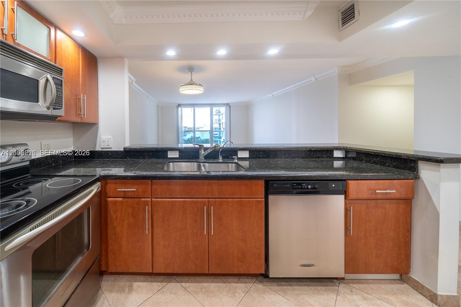 Kitchen featuring wood-finish cabinetry, stone-surface countertops, stainless steel appliances, tile flooring, and recessed lighting