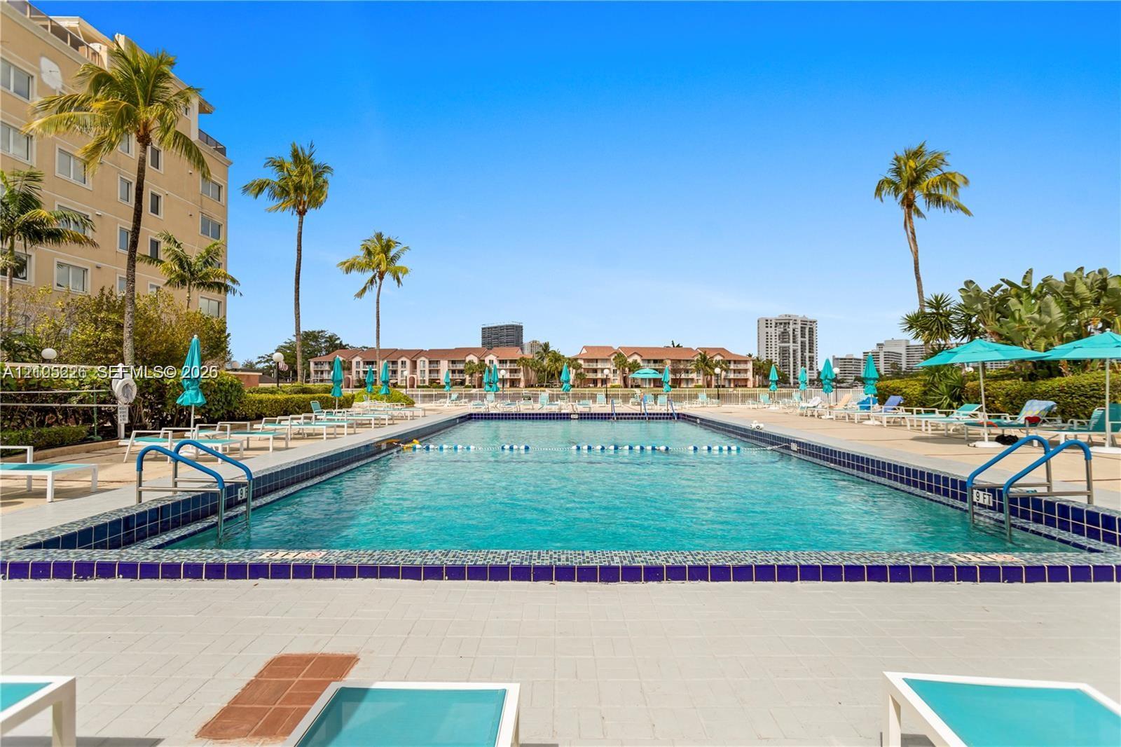 In-ground swimming pool featuring a dark tile border, metal handrails, a paved pool deck, and landscaped surroundings