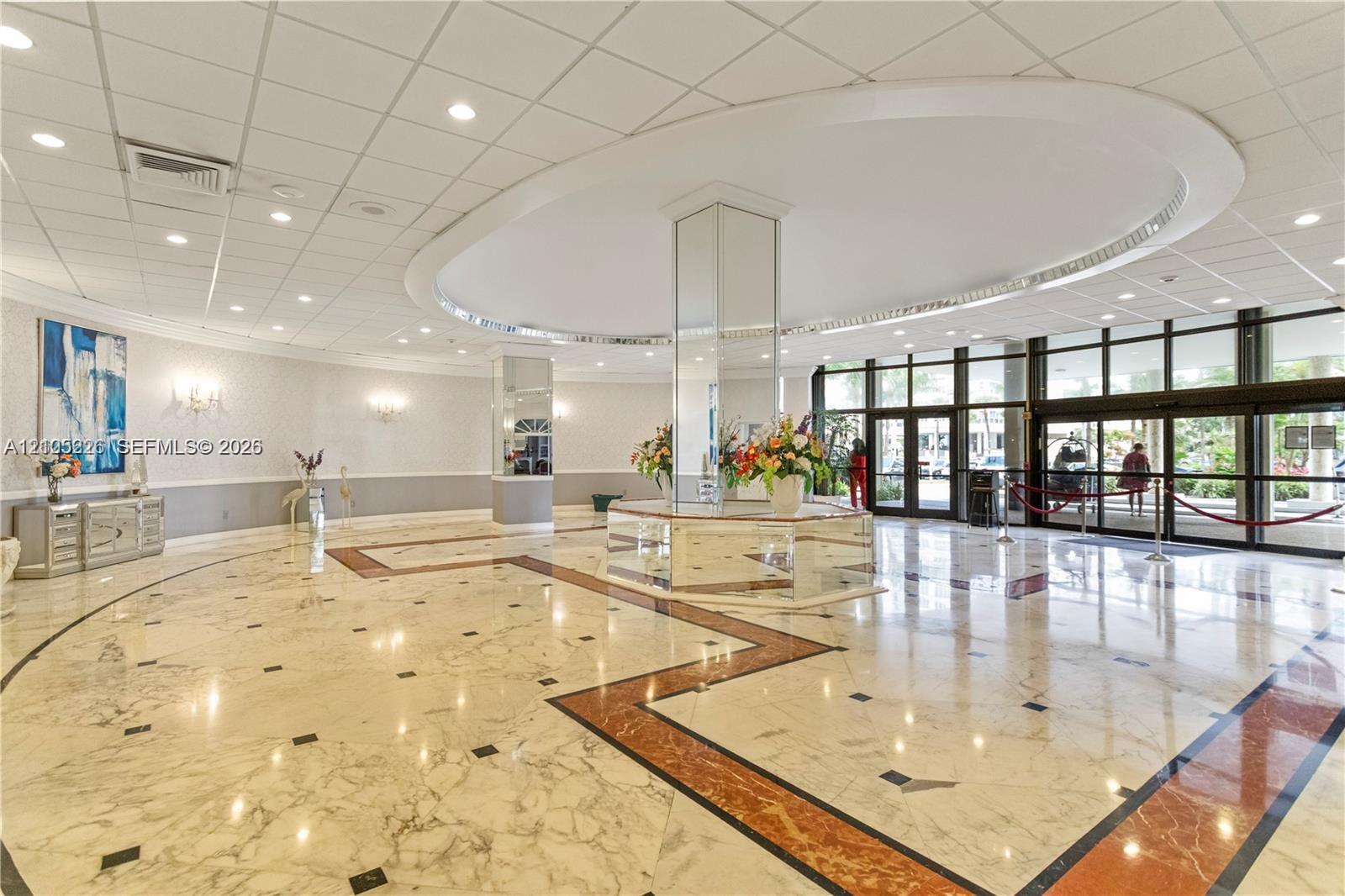 Polished stone flooring with dark stone inlay borders, decorative wallpaper with chair rail molding, and recessed ceiling lighting