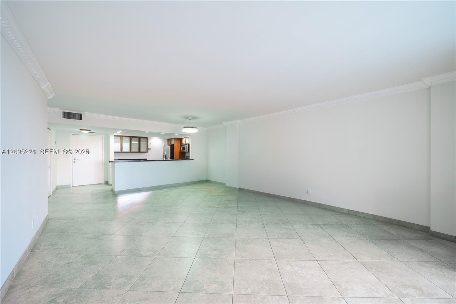 Open-concept living space featuring large-format tile flooring, crown molding, a decorative ceiling fixture, and a sliding glass door providing external access