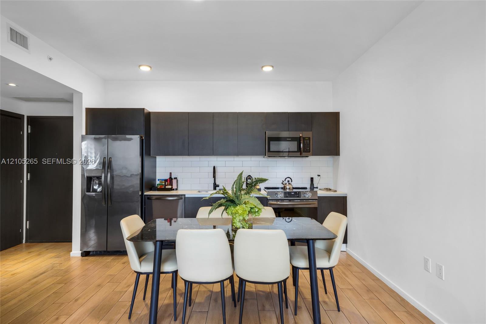Kitchen featuring flat-panel cabinetry, a white subway tile backsplash, stainless steel appliances, and wood-finish flooring