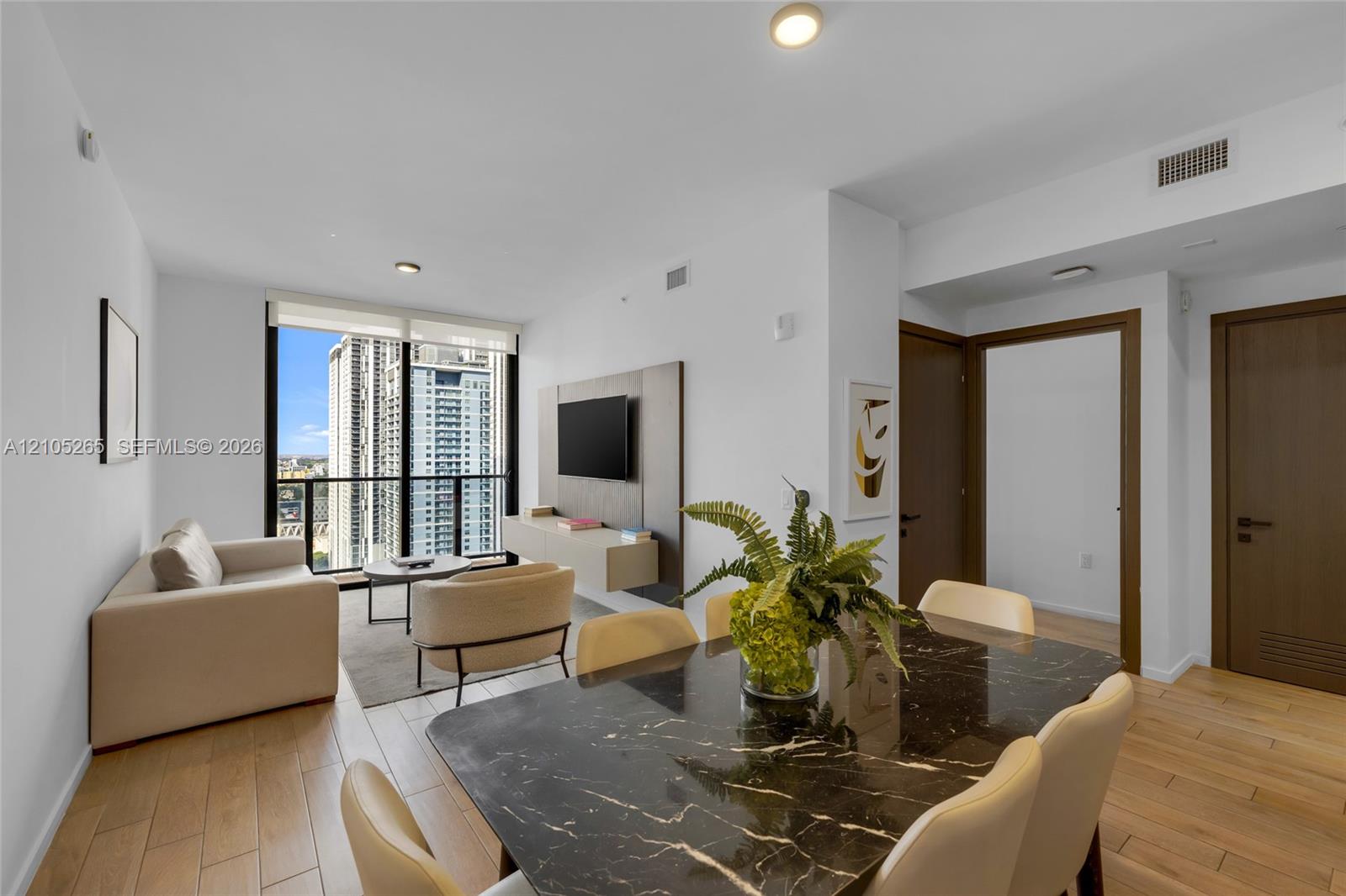 Open-concept living space featuring wood-finish flooring, floor-to-ceiling windows, and a built-in wall-mounted media console
