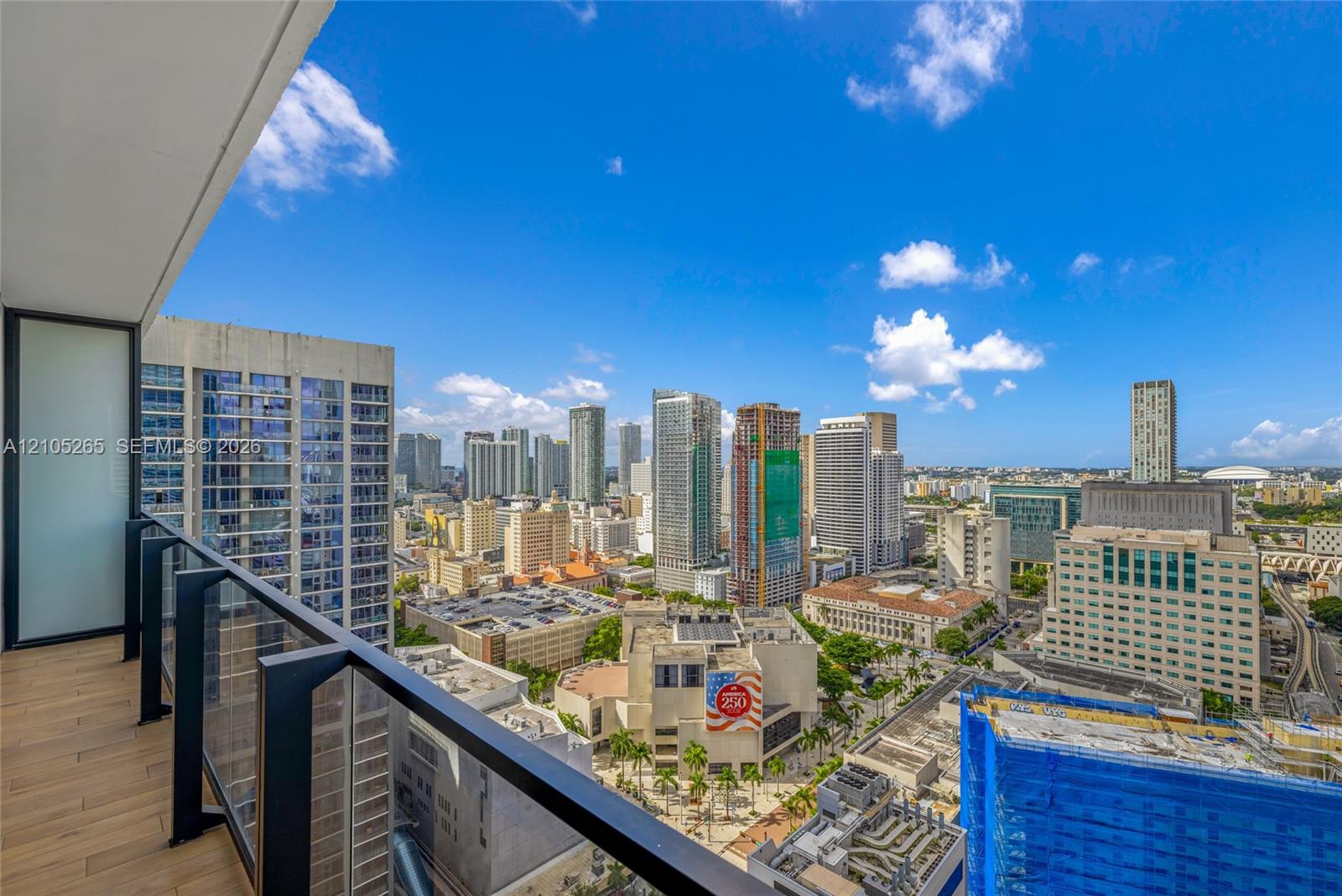 Private balcony featuring wood-finish flooring and a tempered glass railing, showcasing an expansive urban skyline