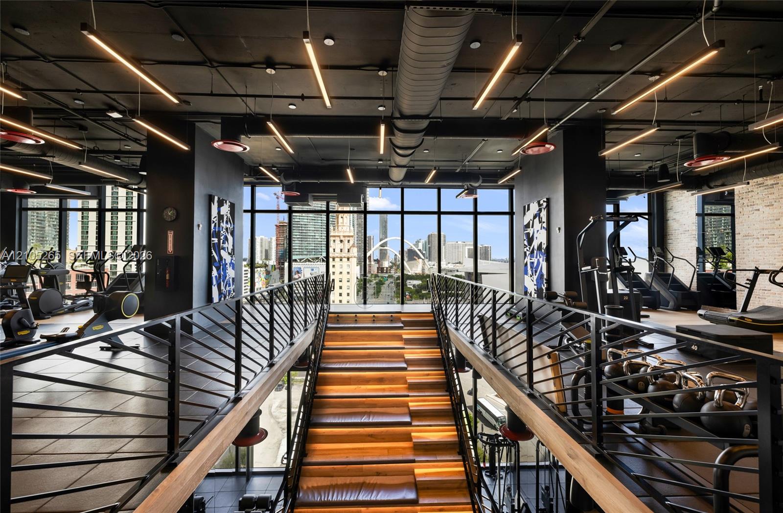 Industrial-style fitness center featuring an open-concept layout, floor-to-ceiling glass windows, exposed ductwork, wood-tread staircase with integrated lighting, and matte black metal railings