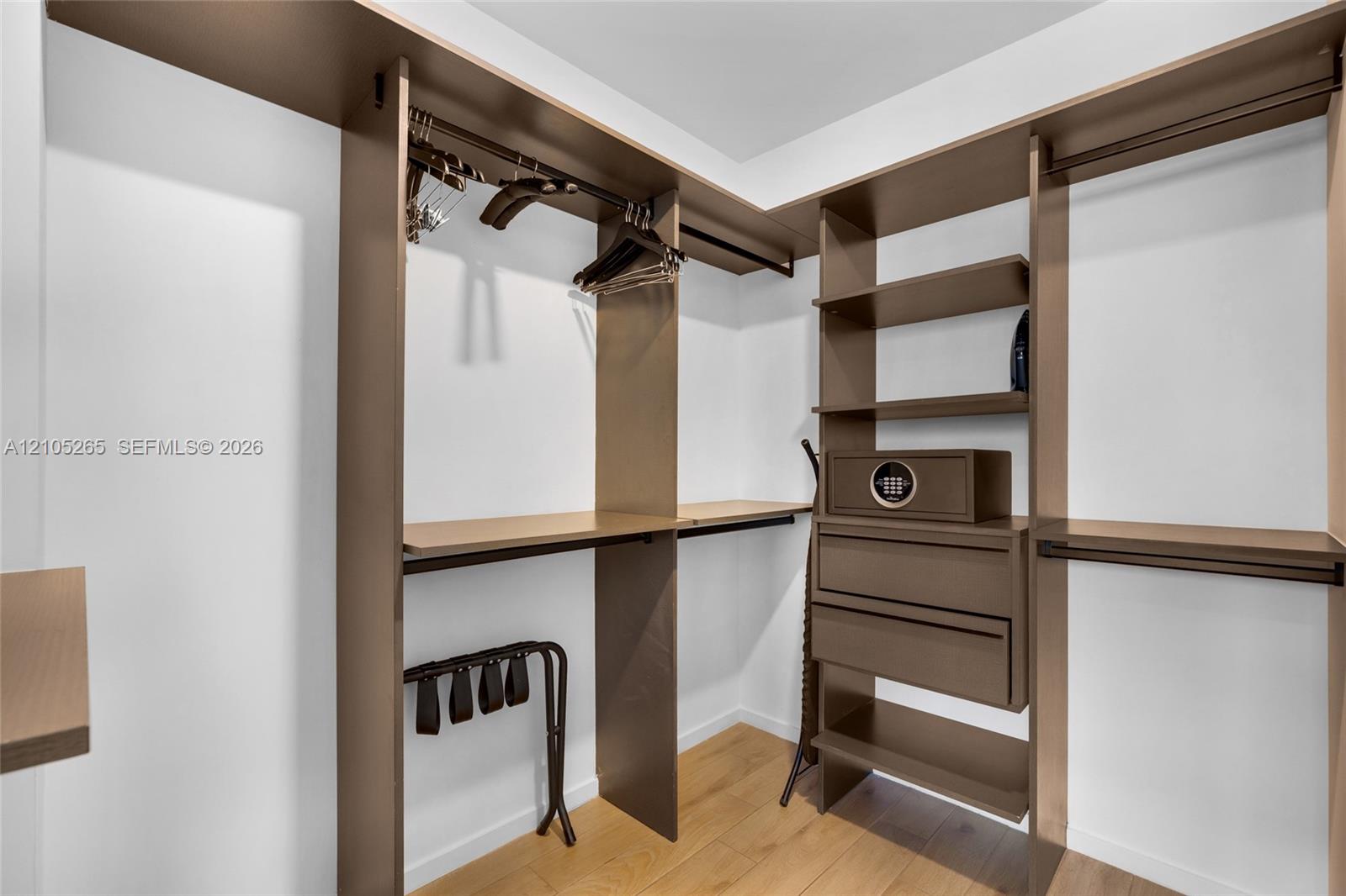 Walk-in closet featuring custom laminate shelving, integrated hanging rods, built-in drawer storage, and wood-finish flooring