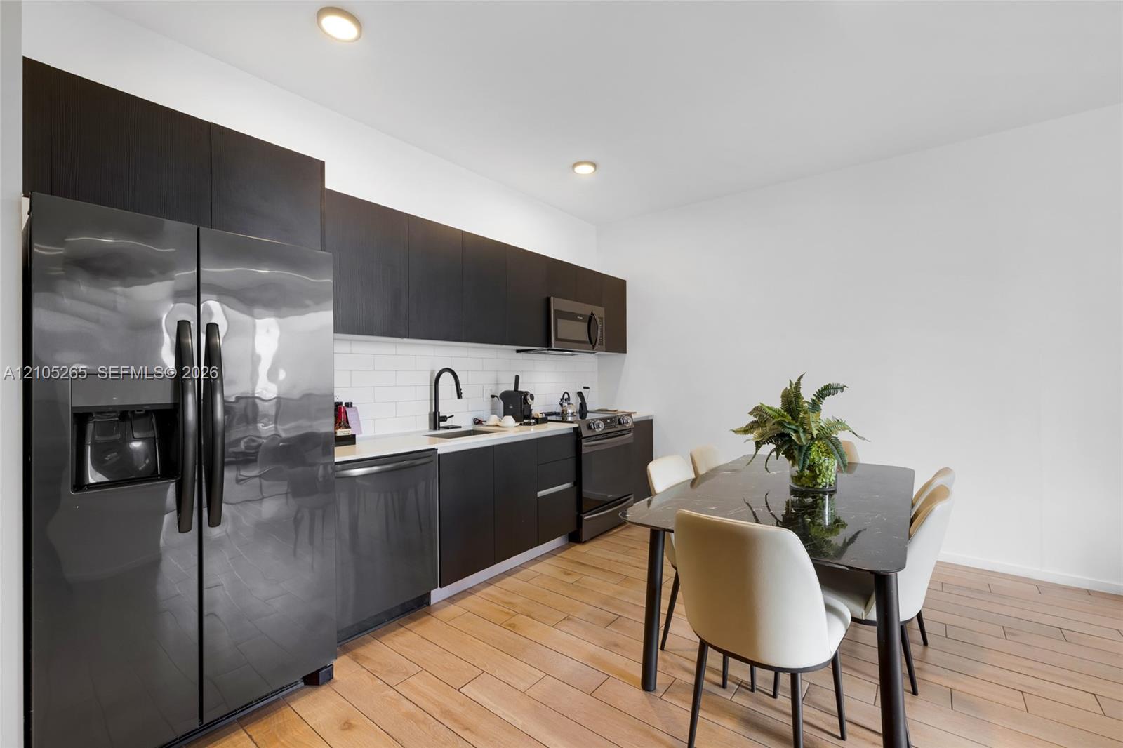 Kitchen featuring flat-panel dark cabinetry, white subway tile backsplash, light-toned wood-finish flooring, and black matte faucet hardware
