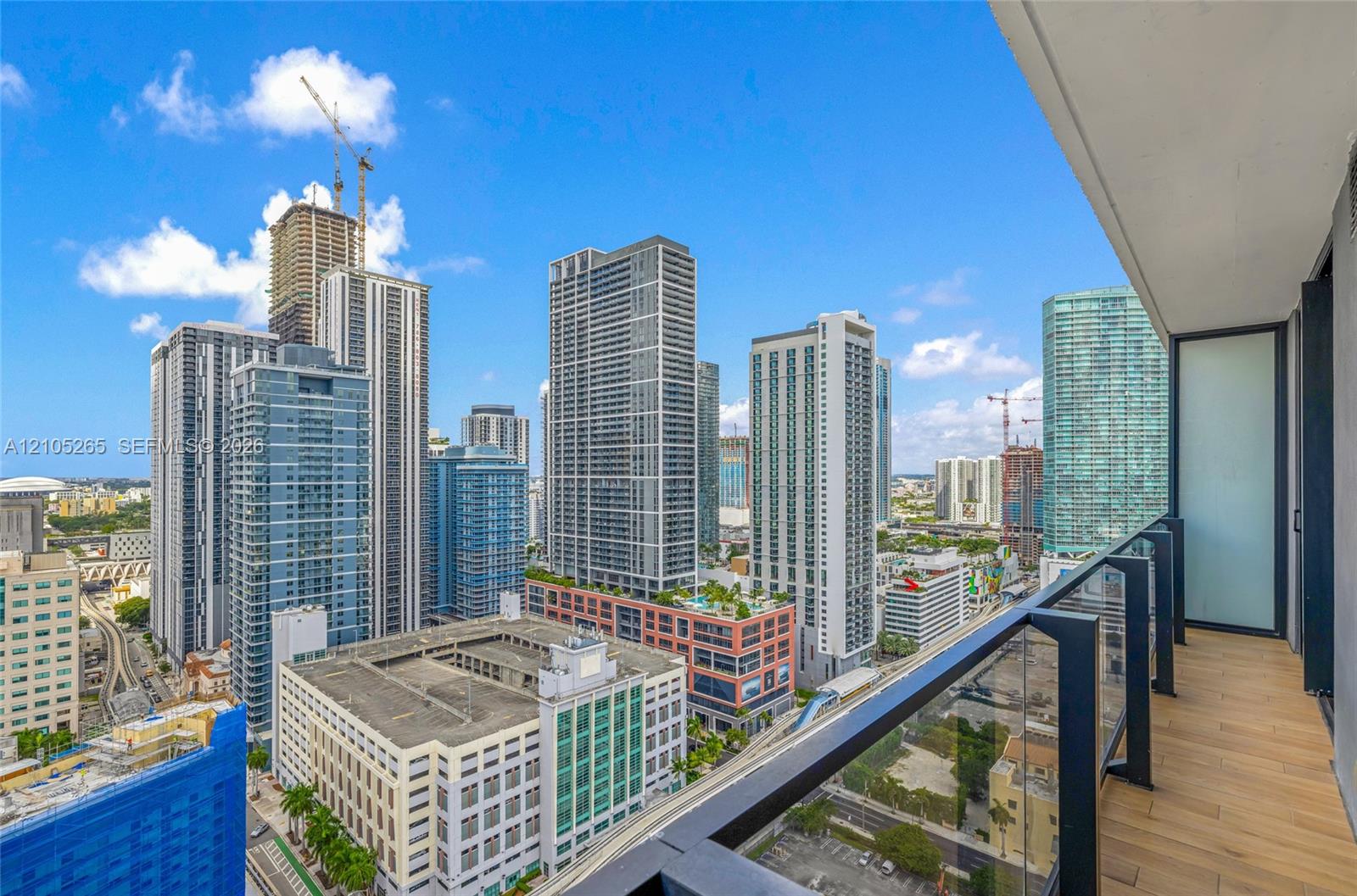 Private balcony with wood-finish flooring, glass and matte black metal railing, and cityscape panorama