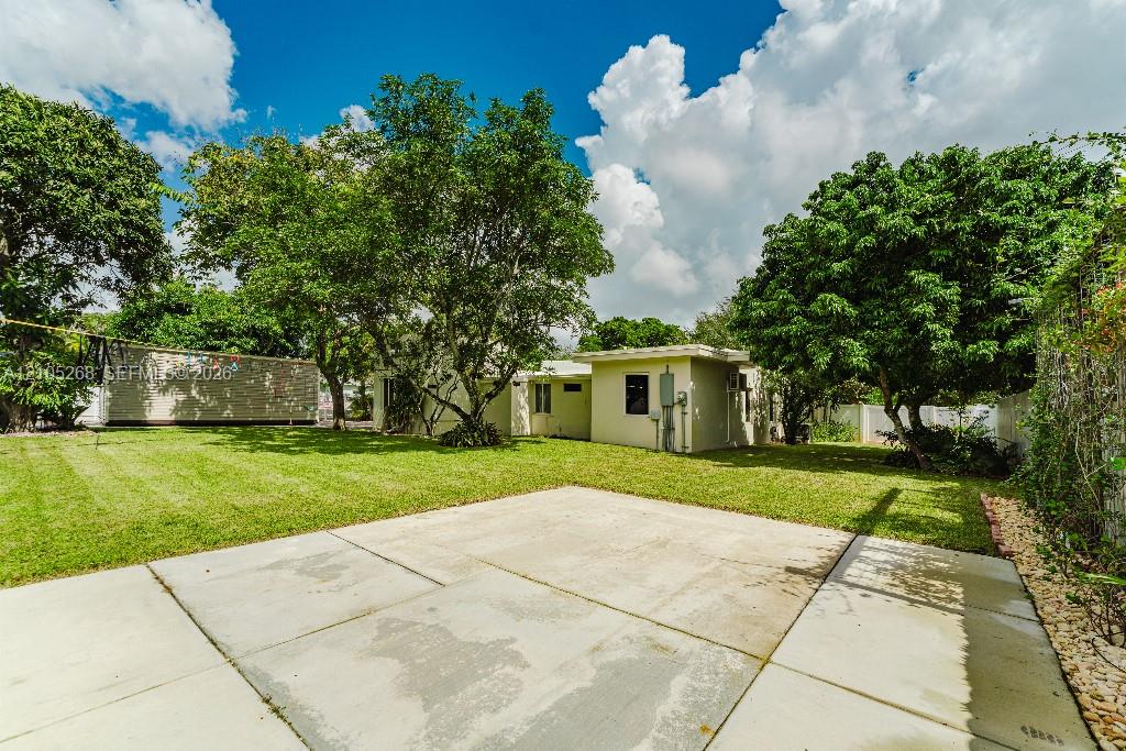 Expansive concrete patio with a lush green lawn and mature trees