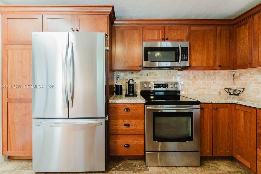 Stainless steel French door refrigerator, wood cabinetry, stainless steel microwave, stainless steel electric range, and light-toned mosaic tile backsplash
